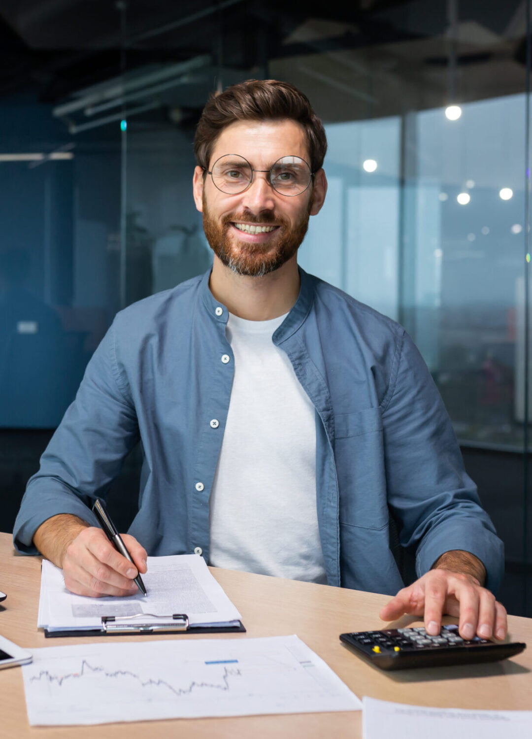 Portrait of successful businessman behind paper work, man in shirt smiling and looking at camera, financier boss inside office using laptop in work at workplace.